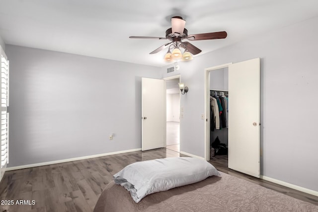 bedroom featuring a spacious closet, wood finished floors, baseboards, and visible vents