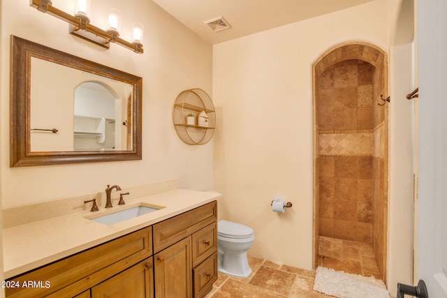 bathroom featuring a tile shower, vanity, and toilet