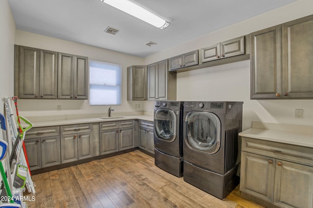 laundry area featuring wood-type flooring, separate washer and dryer, cabinets, and sink