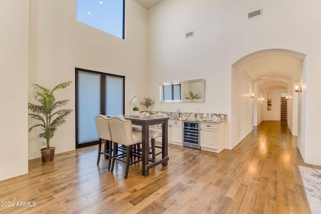 dining space with a high ceiling, beverage cooler, and light hardwood / wood-style floors