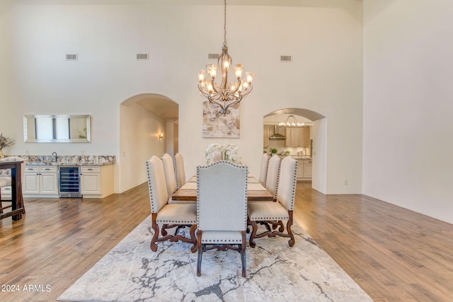 dining room featuring wine cooler, light hardwood / wood-style flooring, sink, and a high ceiling