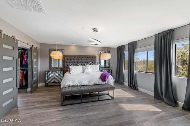 bedroom featuring a barn door, baseboards, visible vents, wood finished floors, and a spacious closet