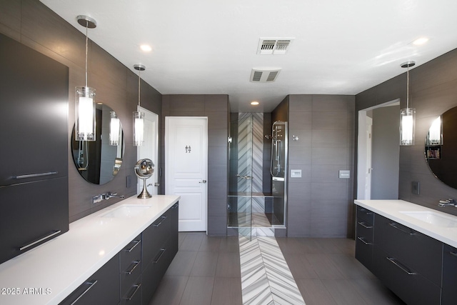 bathroom featuring a tile shower, a sink, visible vents, and tile walls