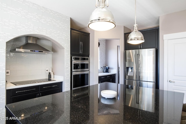 kitchen with tasteful backsplash, dark stone counters, wall chimney exhaust hood, appliances with stainless steel finishes, and decorative light fixtures