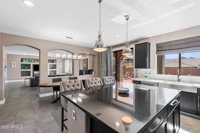 kitchen with decorative backsplash, dark stone countertops, dark cabinetry, pendant lighting, and a sink