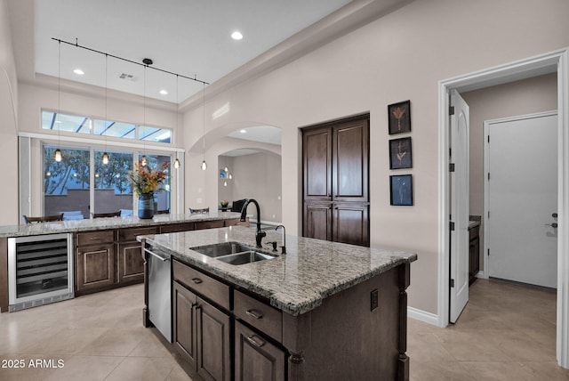 kitchen with light stone countertops, sink, wine cooler, a kitchen island with sink, and dark brown cabinets