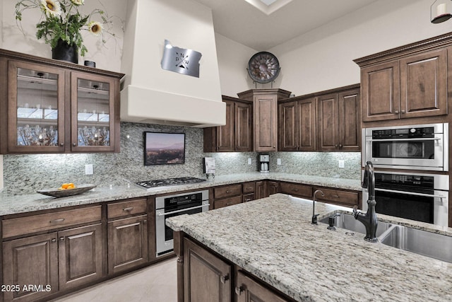 kitchen featuring dark brown cabinetry, light stone countertops, custom range hood, and stainless steel gas cooktop