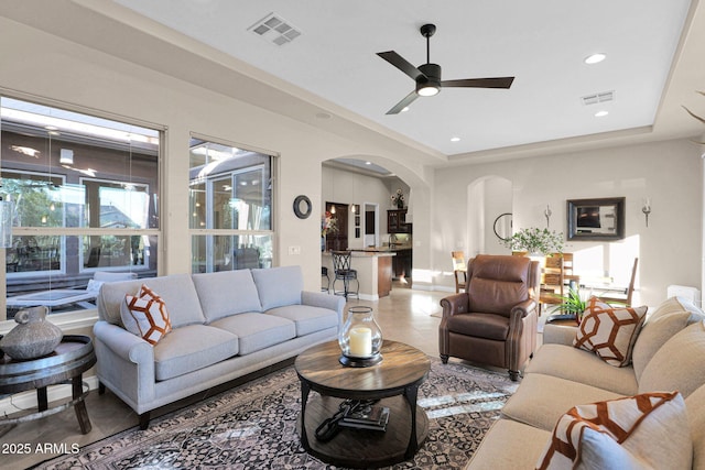 tiled living room with ceiling fan and a tray ceiling