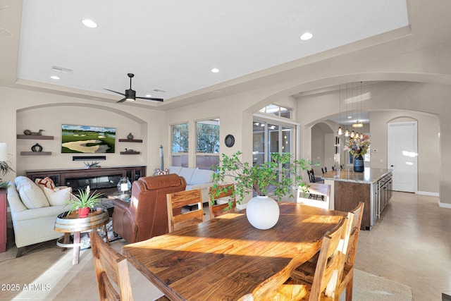 tiled dining space featuring ceiling fan with notable chandelier and a raised ceiling