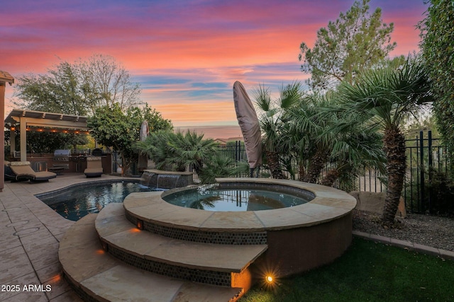 pool at dusk featuring an in ground hot tub, an outdoor kitchen, and grilling area