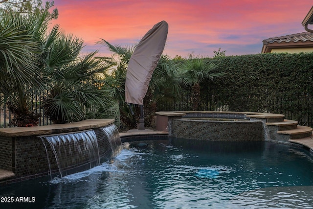 pool at dusk with pool water feature and an in ground hot tub