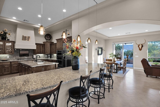 kitchen with decorative backsplash, custom range hood, a spacious island, sink, and decorative light fixtures