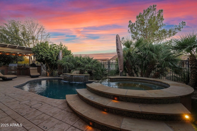 pool at dusk featuring an in ground hot tub, an outdoor kitchen, pool water feature, and a patio area