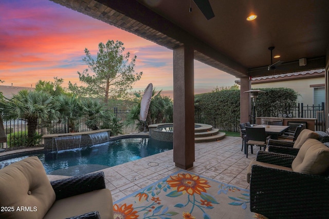 pool at dusk featuring pool water feature, ceiling fan, a patio area, and an in ground hot tub