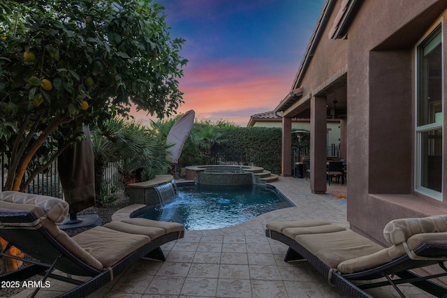 pool at dusk with an in ground hot tub, pool water feature, and a patio