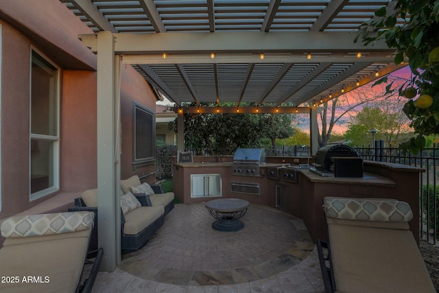 patio terrace at dusk featuring exterior kitchen, area for grilling, and a pergola