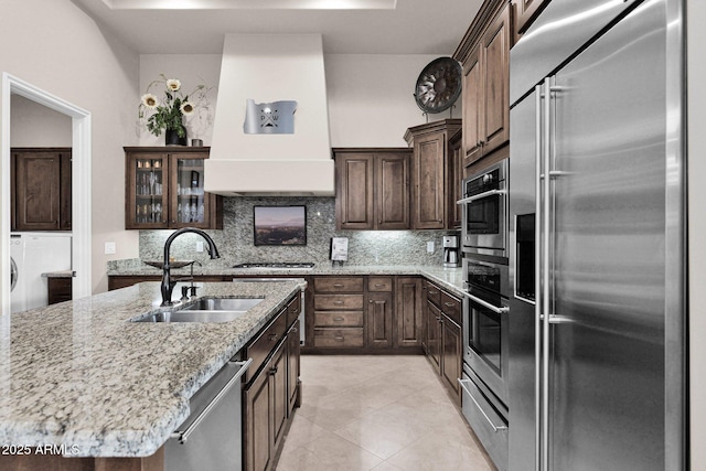 kitchen featuring sink, decorative backsplash, an island with sink, custom range hood, and stainless steel appliances