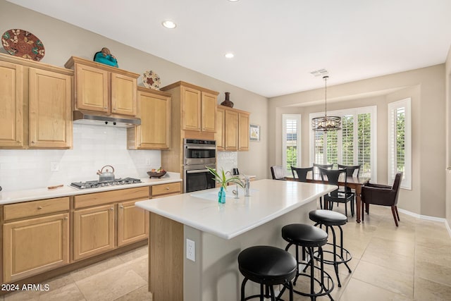 kitchen with under cabinet range hood, appliances with stainless steel finishes, light countertops, and a center island