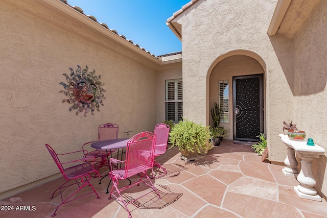 doorway to property with outdoor dining space, a tile roof, a patio area, and stucco siding