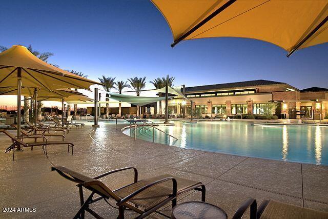 pool at dusk featuring a patio area and a community pool