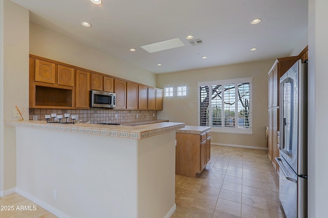 kitchen with appliances with stainless steel finishes, a skylight, tasteful backsplash, a center island, and kitchen peninsula