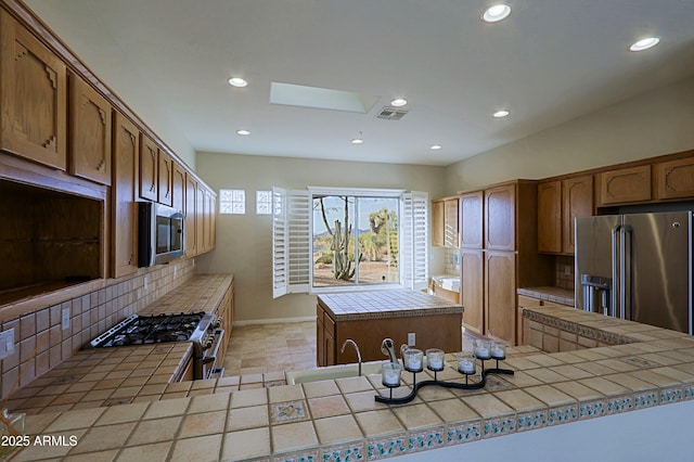 kitchen with backsplash, a skylight, premium appliances, a kitchen island, and tile countertops