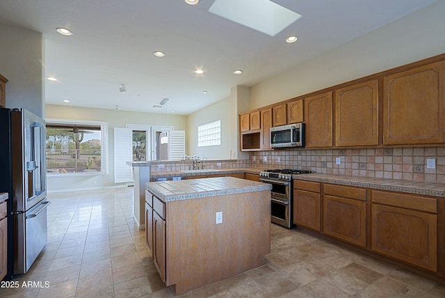 kitchen with a skylight, a center island, appliances with stainless steel finishes, tile counters, and backsplash