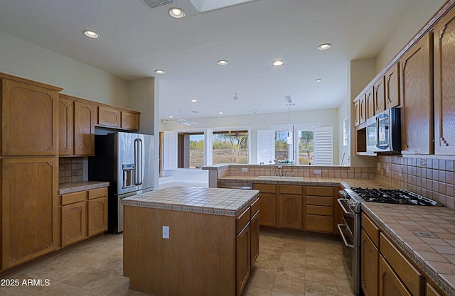 kitchen with a kitchen island, tile countertops, sink, kitchen peninsula, and stainless steel appliances