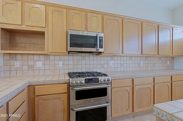 kitchen featuring backsplash, tile countertops, light brown cabinets, and appliances with stainless steel finishes