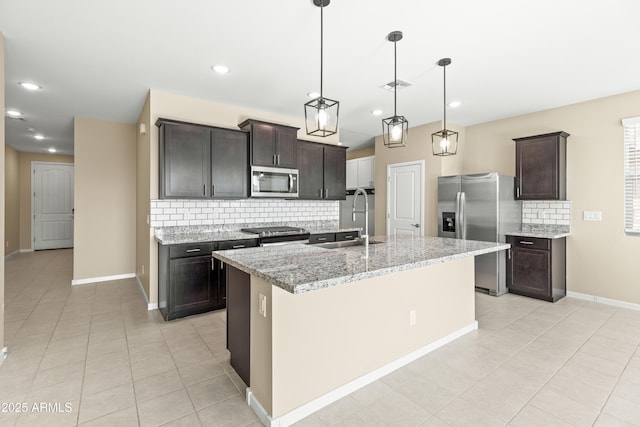 kitchen with sink, light stone countertops, an island with sink, dark brown cabinets, and stainless steel appliances