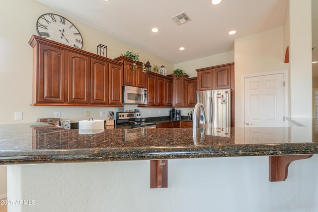 kitchen with dark stone countertops, visible vents, appliances with stainless steel finishes, a kitchen breakfast bar, and a peninsula