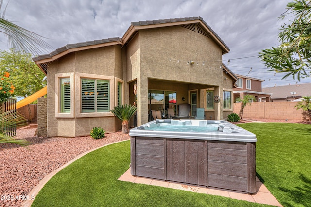back of house featuring a lawn, a fenced backyard, stucco siding, and a hot tub