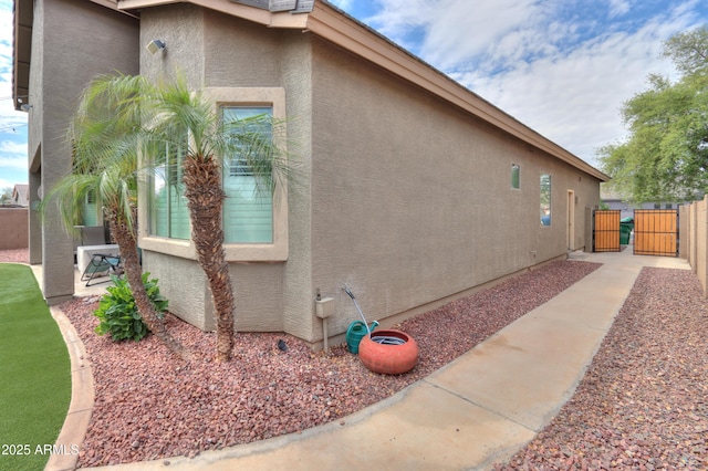 view of home's exterior with stucco siding, fence, and a gate