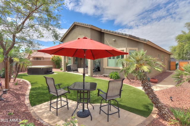 rear view of property featuring a patio, stucco siding, a fenced backyard, a hot tub, and a yard