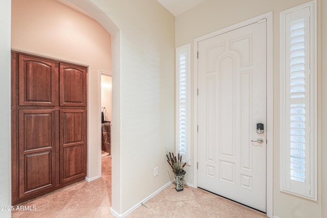 foyer with baseboards, arched walkways, and light tile patterned flooring