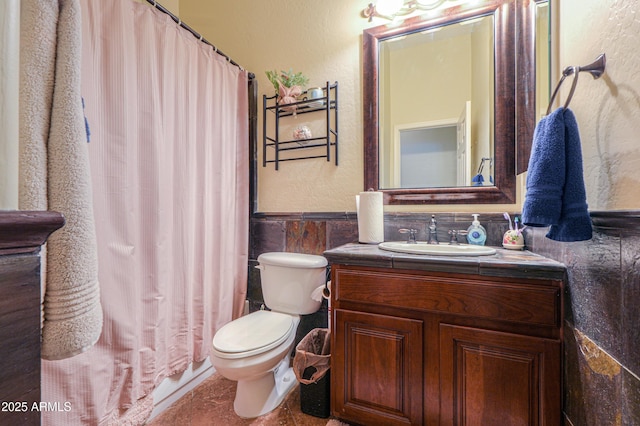 full bath with vanity, curtained shower, toilet, a wainscoted wall, and tile walls