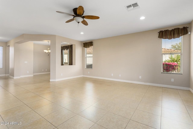 tiled spare room featuring ceiling fan with notable chandelier