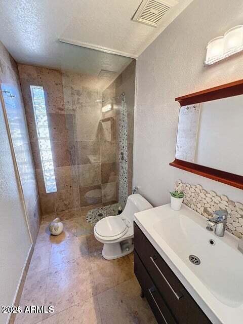 bathroom with a tile shower, vanity, and toilet