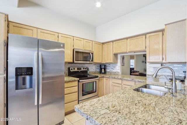 kitchen featuring stainless steel appliances, light brown cabinets, a sink, tasteful backsplash, and light tile patterned floors