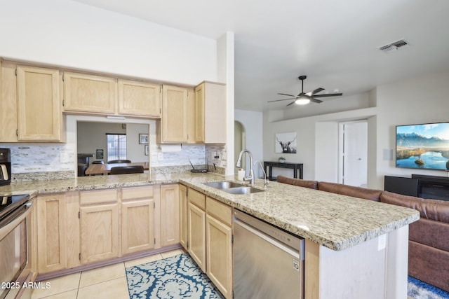 kitchen with stainless steel appliances, light brown cabinets, open floor plan, a sink, and tasteful backsplash