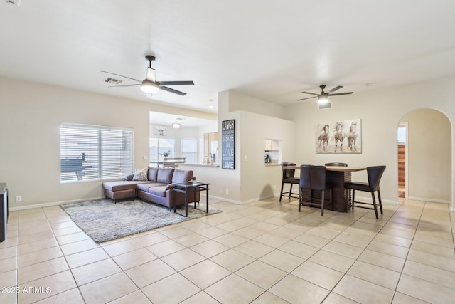 living area with ceiling fan, arched walkways, light tile patterned floors, and baseboards