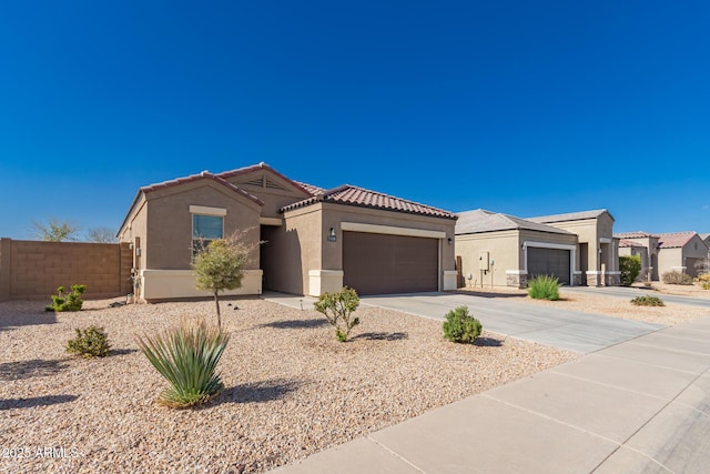 view of front of property featuring stucco siding, driveway, a tile roof, fence, and a garage