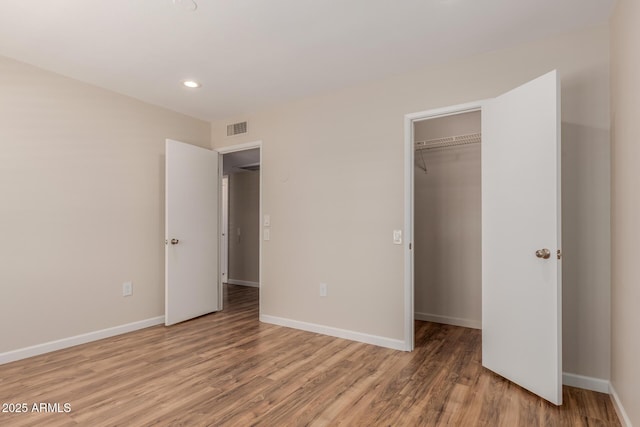 unfurnished bedroom featuring a walk in closet, wood-type flooring, and a closet