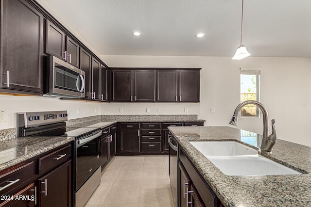 kitchen featuring dark brown cabinetry, light tile patterned flooring, a sink, dark stone countertops, and stainless steel appliances