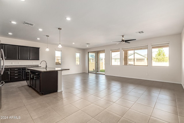 kitchen with light stone countertops, sink, ceiling fan, pendant lighting, and a kitchen island with sink