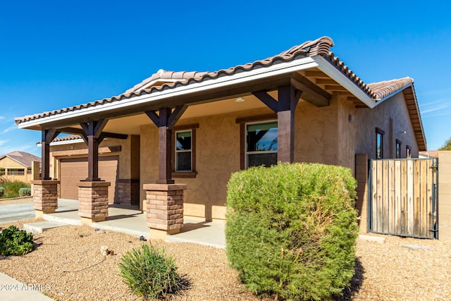 exterior space with covered porch, a garage, a tile roof, and stucco siding