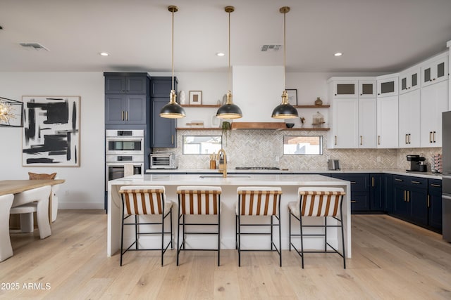 kitchen featuring hanging light fixtures, glass insert cabinets, white cabinets, a sink, and blue cabinets