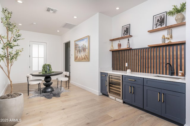 bar featuring light wood finished floors, visible vents, a sink, wet bar, and beverage cooler