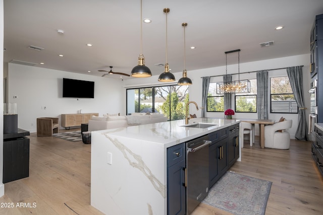 kitchen featuring decorative light fixtures, a sink, visible vents, and an island with sink