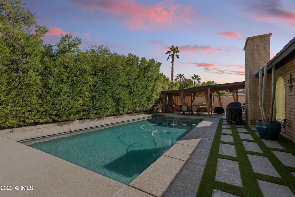 pool at dusk featuring a patio area and a grill